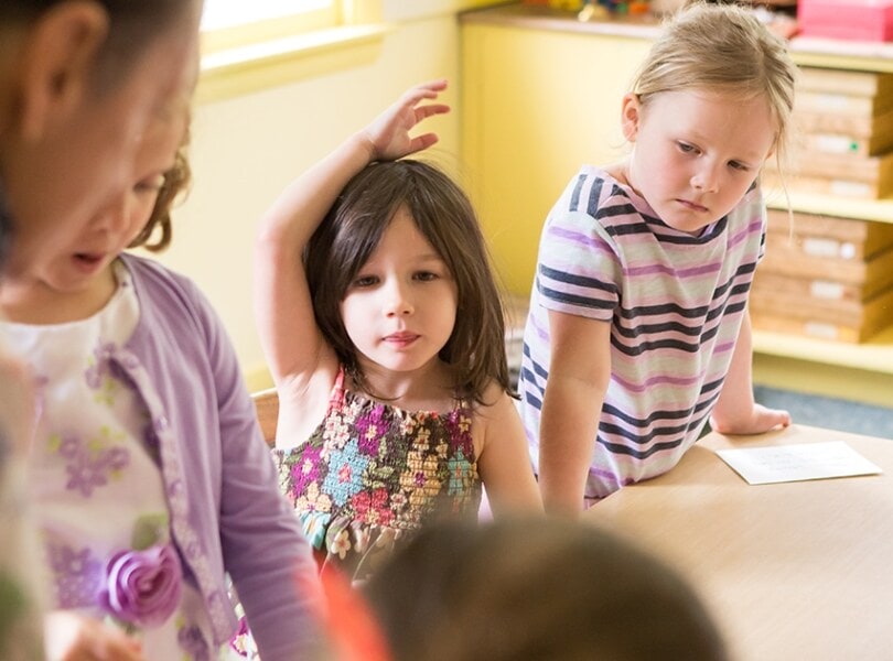 A little girl raises her hand in Sunday School