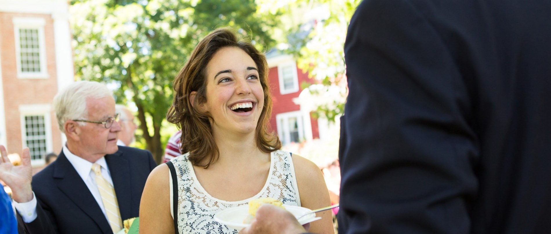 A twenty-something woman talks with an older gentleman who is eating cake.