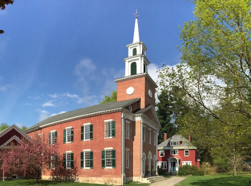 Exterior image of the historic 1824 congregational church in Stockbridge. A brick building with green shutters and a tall white steeple.
