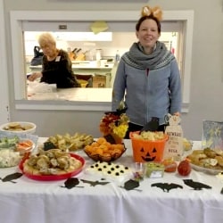 A woman in a costume behind a buffet of Halloween snacks