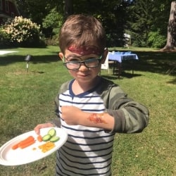 A child with pirate face painting enjoys a snack on the lawn