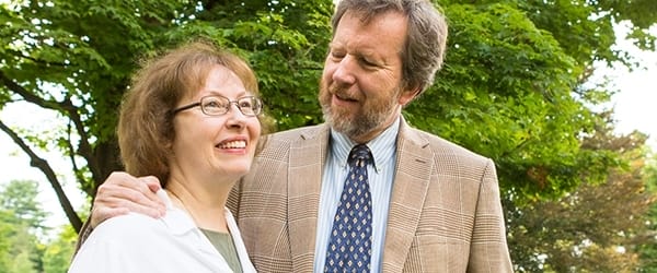 A wife and husband smile on the green in front of the church